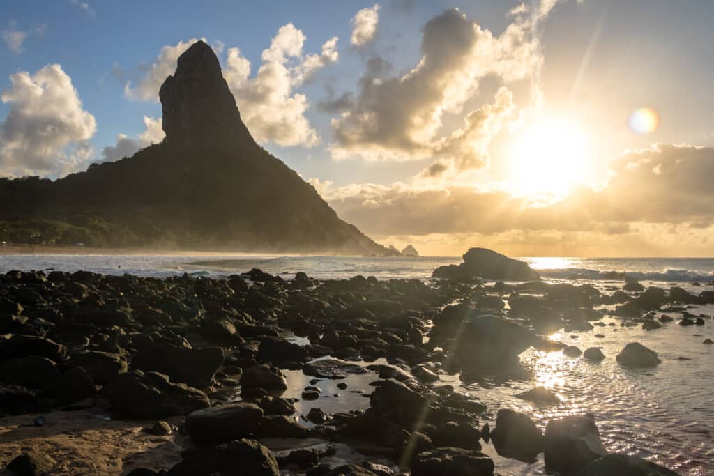 Pôr do sol na Praia da Conceição com o Morro do Pico ao fundo em Fernando de Noronha, Pernambuco, Brasil. (Foto: diegograndi/Envato)