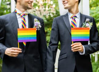 Argumentos a favor do casamento gay Casal de homens celebrando o seu casamento gay, cada um segundo pequenas bandeiras do arco-íris.
